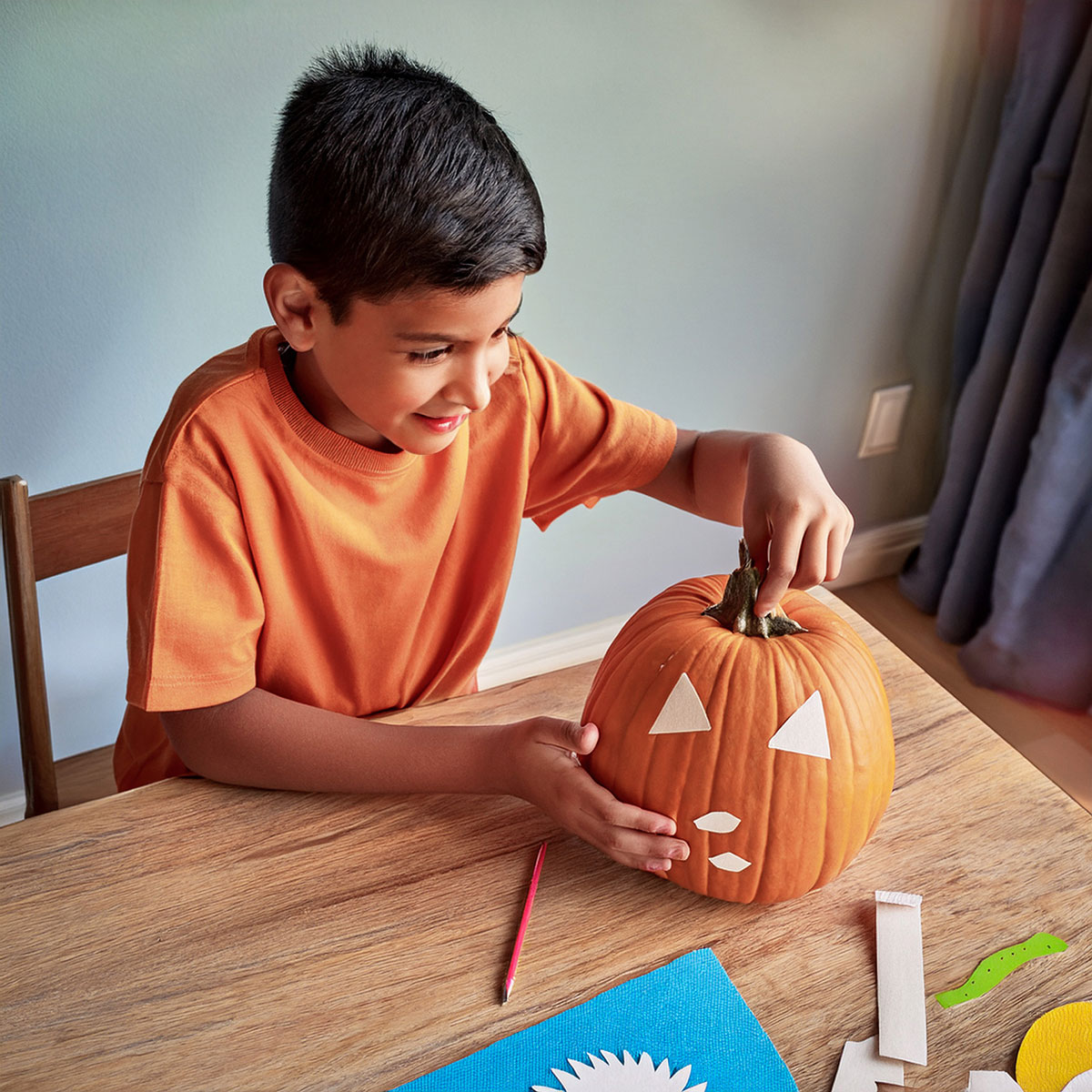 Child decorating pumpkin with paper cutouts at table