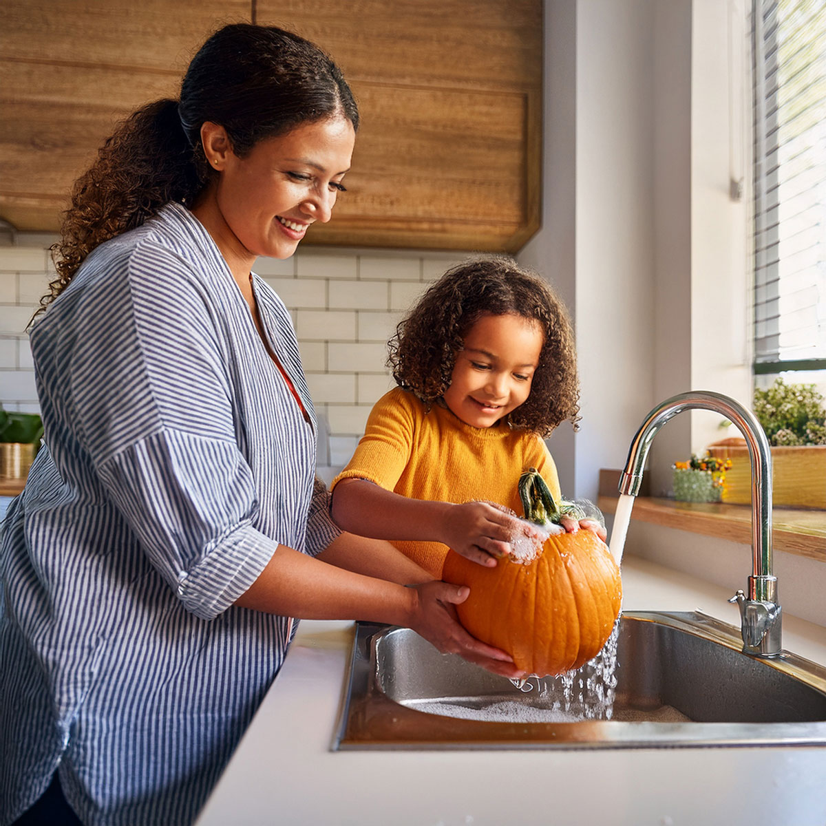 Woman and child washing a pumpkin together in kitchen