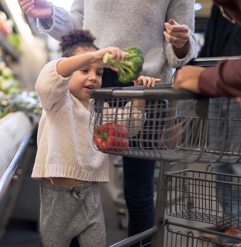 Child placing broccoli into shopping cart