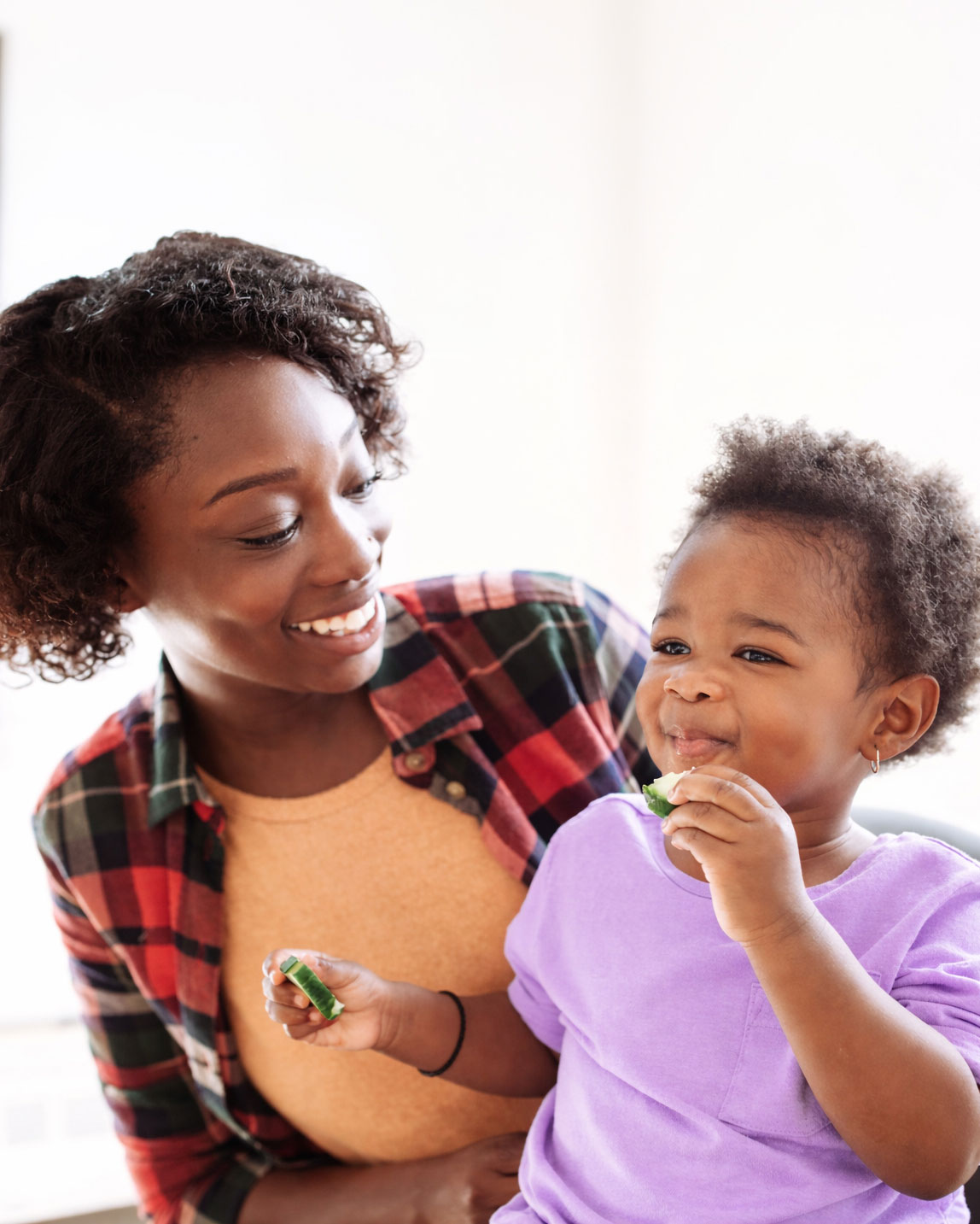 Mother smiling at toddler eating cucumber