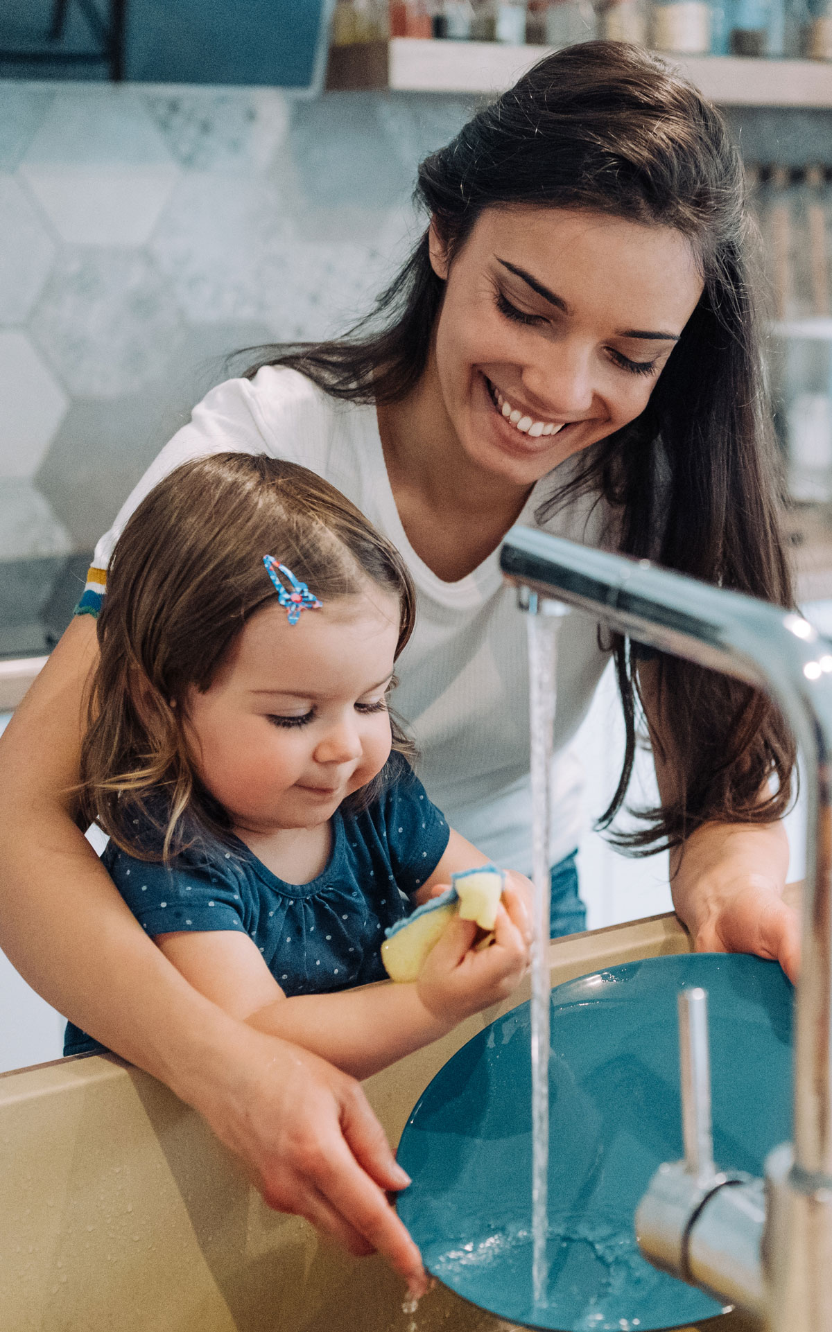Mother and daughter washing dishes together, smiling