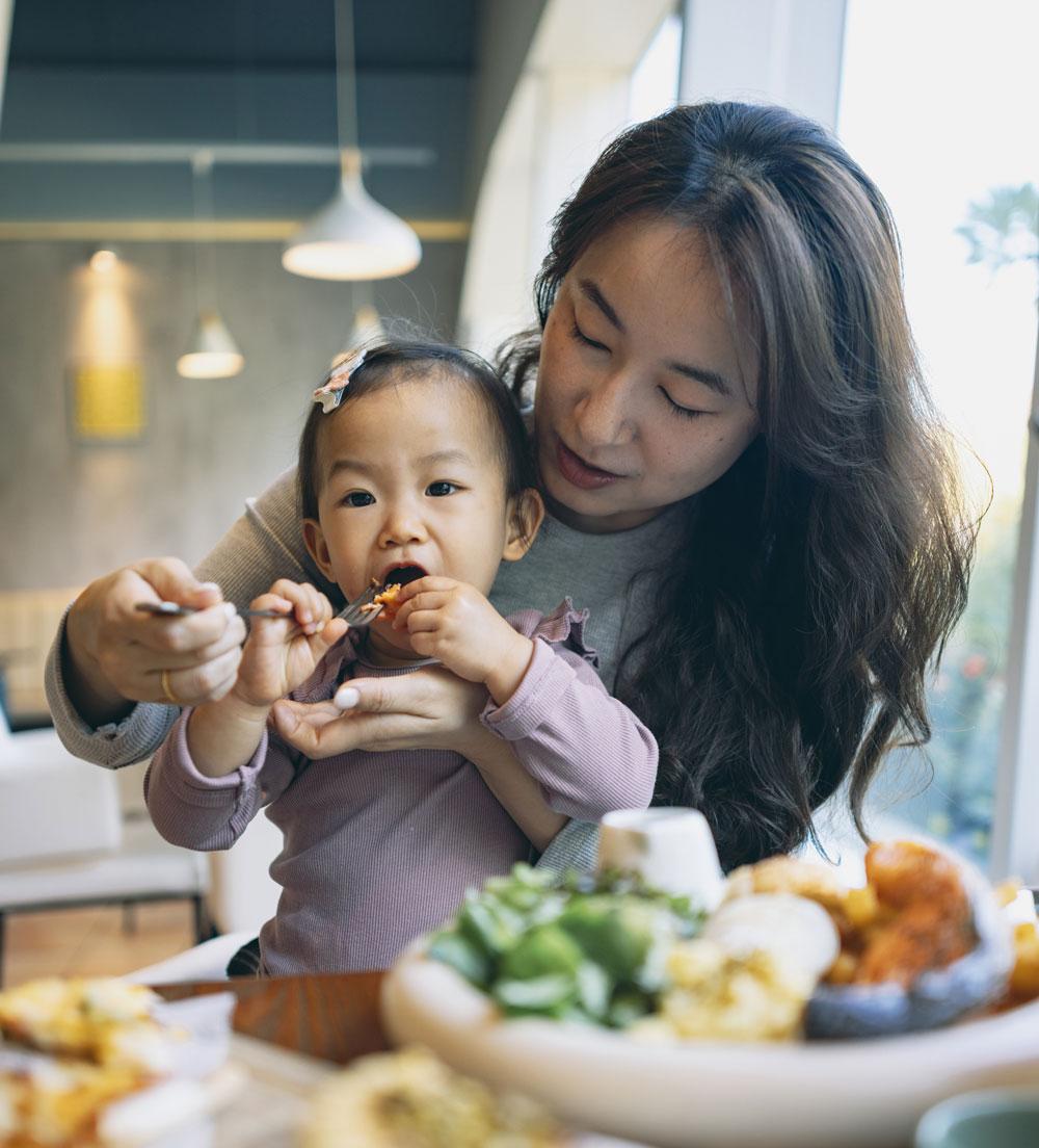 Mother feeding toddler at a table full of food