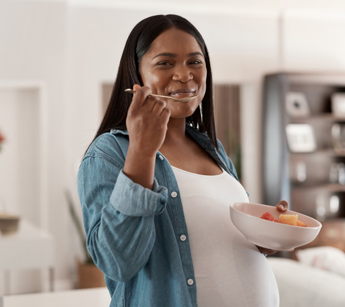 Pregnant woman enjoying fruit salad at home.