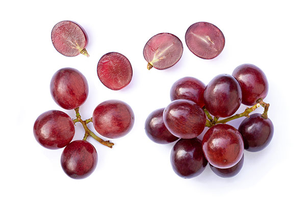 Red grapes with cut halves displayed on white background.
