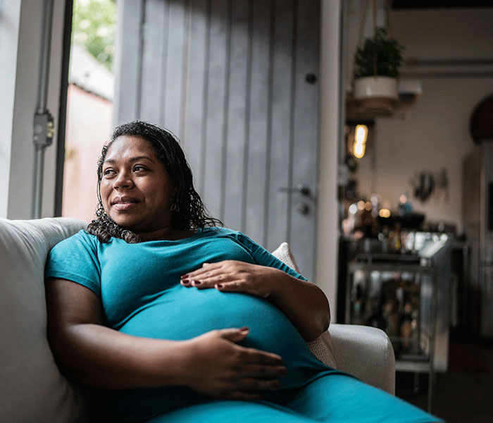 Pregnant woman sitting on a couch, smiling gently.