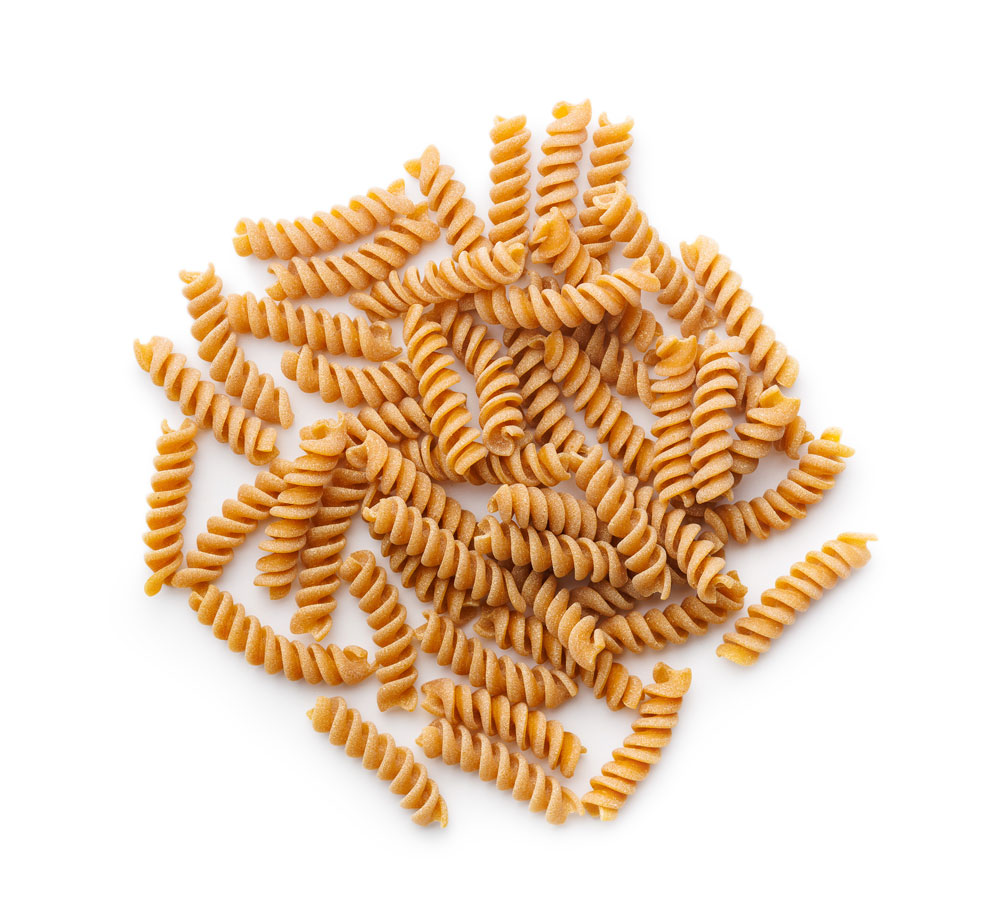 Whole wheat fusilli pasta scattered on white background