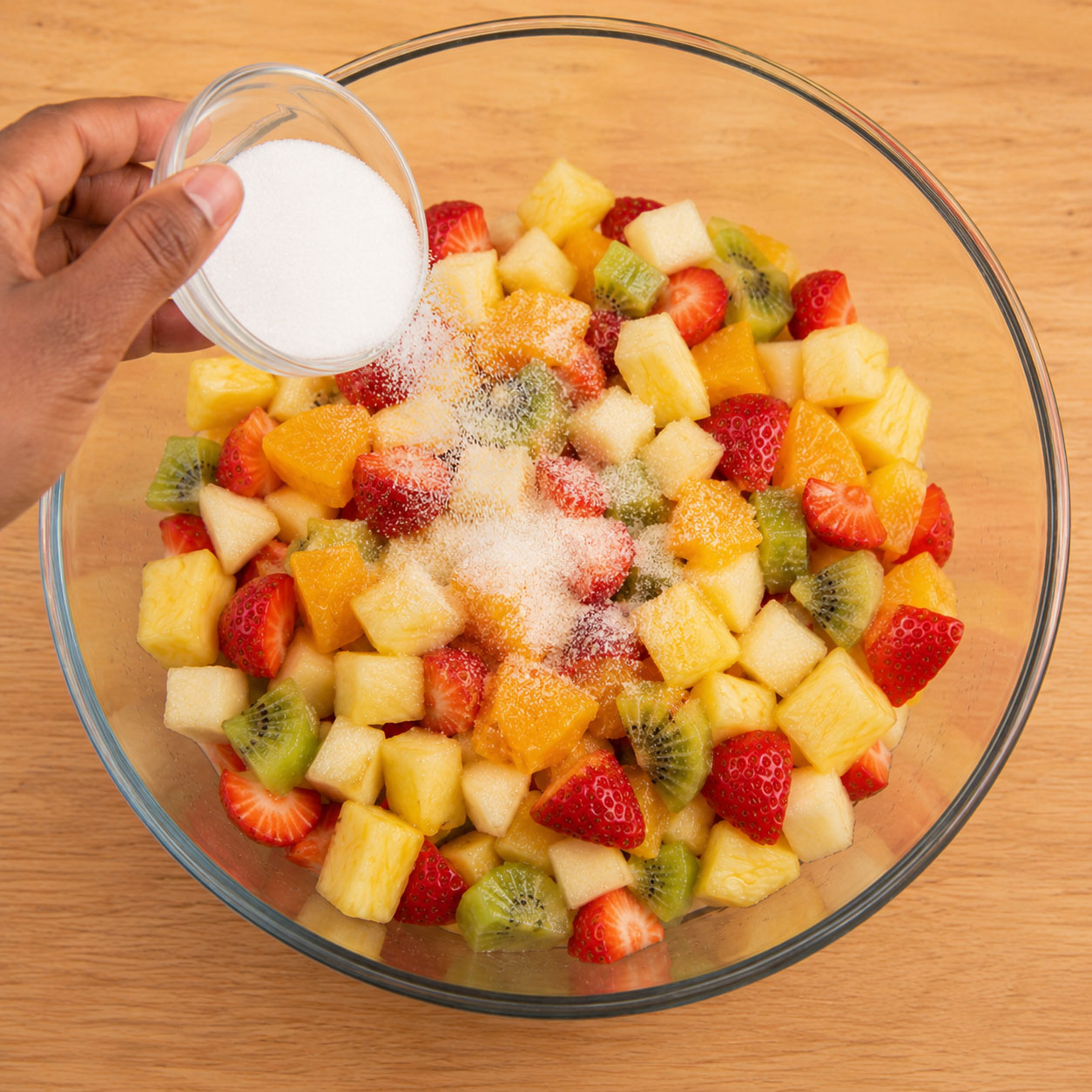 Sprinkling sugar over a bowl of chopped fruit
